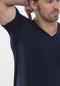 T-shirt bleu marine à col en V fabriqué en tissu doux et texturé, avec des manches courtes et une coupe ajustée, dotée de détails de couture visibles.