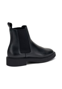 Botín Chelsea de cuero negro con panel lateral elástico y tirador, que presenta una puntera redonda y una suela de goma gruesa y texturizada.