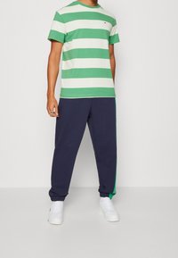 Grön och vit randig T-shirt med korta ärmar, kombinerad med mörkblå sweatpants med gröna sidodetaljer och vita sneakers.