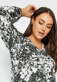 Svart och vit blommig blus med långa, puffärmar, V-ringning och textil med struktur. Har en knappdetalj fram.