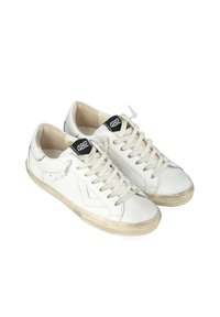 Sneakers bianche in pelle con accenti beige, punta tonda, lacci piatti e una patch nera con logo sulla linguetta. Suola in gomma leggermente usurata.