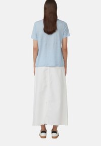 Lichtblauw T-shirt met korte mouwen gecombineerd met een witte maxi-rok en witte schoenen met zwarte accenten. Eenvoudig ontwerp, relaxte pasvorm en zachte textuur.