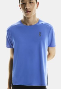 Niebieska koszulka sportowa z krótkim rękawem, wykonana z materiału odprowadzającego wilgoć. Posiada logo na klatce piersiowej oraz zaokrąglony dekolt.