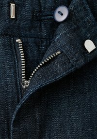 Tissu en denim bleu foncé avec une fermeture éclair argentée partiellement ouverte, un bouton gris et des boutons-pression en métal sur un vêtement.