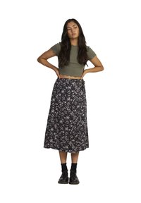 Olive green cropped top with scalloped hem, paired with a black floral midi skirt featuring pink and white patterns. Black lace-up shoes.