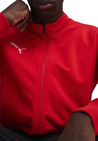 Rote Kapuzenjacke aus weichem Stoff mit einem weißen Puma-Logo auf der linken Brust, mit gerippten Bündchen und hohem Kragen.