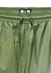 Lys grønne shorts med en tekstureret overflade, der har en elastisk talje, snøre og et sort-hvidt mærke øverst.