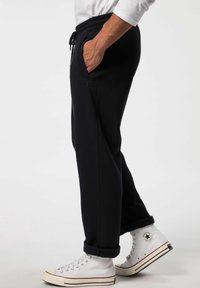 Marinefarbene Sweatpants mit Kordelzugbund, Seitentaschen und gerippten Bündchen, kombiniert mit weißen High-Top-Sneakers mit Logo.