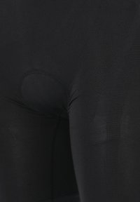 Zwarte sportleggingen van een gladde, rekbare stof, met een verstevigde tailleband en een klein uitsnede detail bij het kruis.