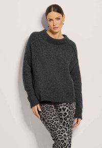 Donkergrijze oversized trui met een brede hals, geribbelde zoom en lange mouwen, gecombineerd met grijze legging met patroon van dierenprint.