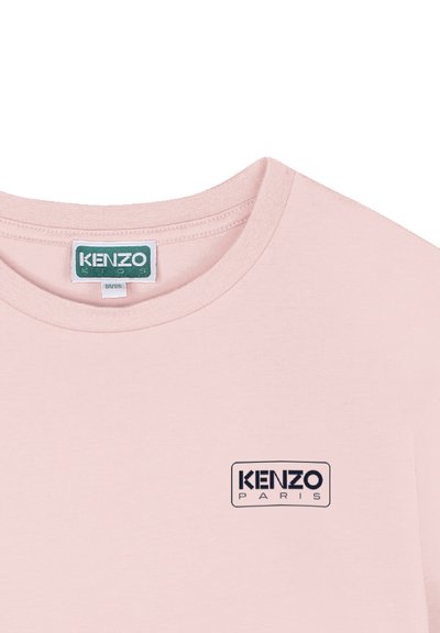 T-shirt en coton rose clair avec col rond. Présente un logo rectangulaire noir avec le texte "KENZO PARIS" sur le devant. Texture lisse.