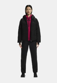 Fekete puffdzseki, rózsaszín kapucnis pulóver és fekete nadrág. A dzseki cipzáros elülső résszel és kapucnival rendelkezik; elegáns és szigetelt kialakítású.