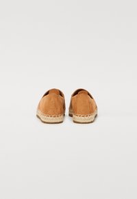 Espadrilles en cuir tan avec une forme arrondie, semelle en jute et coutures minimales. La vue arrière montre une texture lisse et un branding subtil.