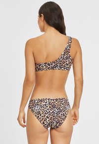 Ensemble de bikini en impression léopard comprenant un haut asymétrique avec des bords festonnés et un bas taille basse assorti, fabriqué à partir d'un tissu lisse et extensible.