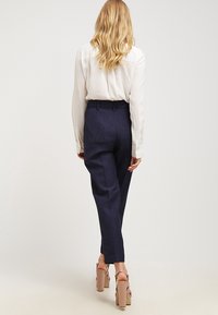 Navy kalhoty na míru s vysokým pasem a rovným střihem, vyrobené z texturované látky. V kombinaci s lehkou blůzou s dlouhým rukávem.