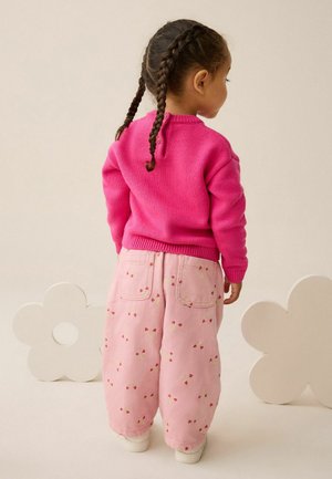 Pulover roz și pantaloni roz cu un model de căpșuni, având o croială lejeră și manșete elastice, purtați cu pantofi albi, văzuți din spate.