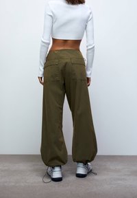 Pantalon cargo à jambes larges en coton vert olive avec deux grandes poches arrière et une taille à cordon, associé à un haut blanc court à manches longues.