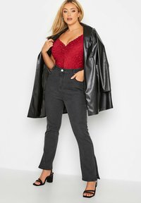 Czarna kurtka z sztucznej skóry noszona na czerwonym body z koronką, w połączeniu z czarnymi dżinsami o wysokim stanie i czarnymi sandałami na obcasie z paskami.