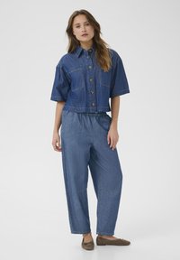 Denim cropped jakke med knaplukning og to brystlommer, sammen med løstsiddende denimbukser med elastisk talje, begge i en mellemblå farve.