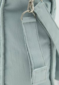 Borsa in tessuto blu chiaro texturizzato con una larga tracolla e hardware argentato, caratterizzata da dettagli di cucitura e una forma rettangolare.