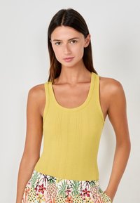 Top giallo a coste con scollatura tonda e spalline larghe, abbinato a una gonna con fantasia floreale dai colori vivaci.