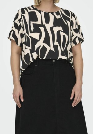 Kobieta ubrana w czarny i beżowy top z abstrakcyjnym wzorem na krótkim rękawie, wpuszczony do wysokiej taliowanej czarnej spódnicy z kieszeniami.