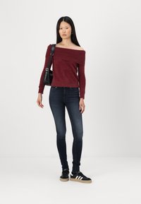 Pulover burgundy cu umerii goi, cu o textură pufoasă, asortat cu blugi skinny negri și adidași negri cu dungi albe.