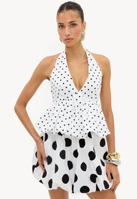 Femme portant un haut dos nu blanc à petits pois noirs et une jupe assortie à gros pois noirs, accessoirisée avec des bracelets et des boucles d'oreilles.