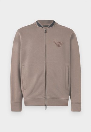 Light brown zip-up sweatshirt with a ribbed collar, side pockets, and an embossed logo on the chest. Soft fabric and relaxed fit.