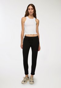 Biały skrócony top na ramiączkach, czarne joggery z elastycznym pasem i beżowe sportowe buty w wzory. Dopasowany fason o gładkich fakturach i subtelnych detalach.