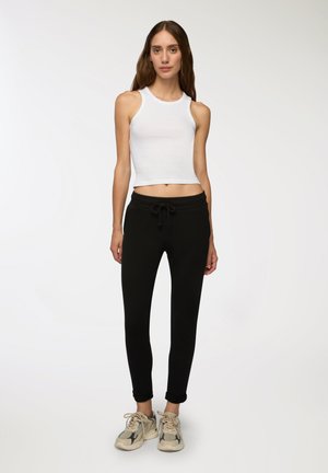 Top corto bianco, pantaloni joggers neri con cintura elastica e sneakers beige con motivi. Design aderente con texture lisce e dettagli sottili.