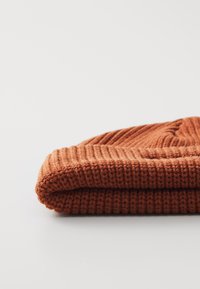 Gehaakte beanie in roestoranje, met een dikke geribde textuur en een opgerolde rand. Zacht wolmateriaal met een naadloos ontwerp.