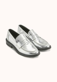Mocassins en cuir argenté avec un accent en nœud, bout arrondi, semelle noire contrastante et texture lisse. Présente des détails de couture classiques.