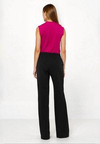 Fuksjowy top bez rękawów w połączeniu z czarnymi szerokimi spodniami z wysokim stanem, wykonanymi z gładkiego materiału z elastycznym pasem.