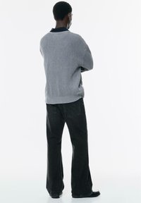 Maglione a righe grigie con colletto blu navy, abbinato a jeans neri a gamba larga. La texture è a costine e la vestibilità è comoda.