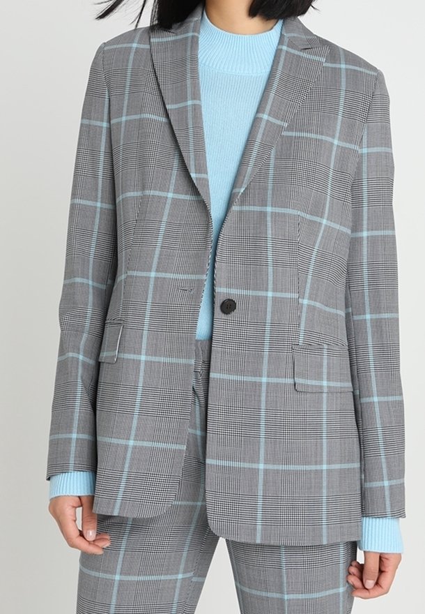 Szary marynarka w kratę z jasnoniebieskimi liniami, z zapięciem na jeden guzik, klapami w stylu notch oraz dwoma przednimi kieszeniami, noszona na jasnoniebieskim swetrze.