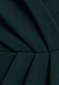 Tejido verde oscuro con una superficie texturizada, que presenta pliegues prominentes que crean un diseño estructurado. Ideal para diversas aplicaciones de vestimenta.