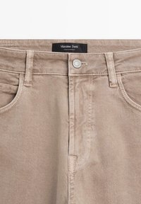 Beżowe dżinsy o prostym kroju, z zapięciem na srebrny guzik, kieszeniami z przodu i przeszyciami wzdłuż pasa.