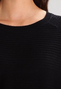 Maglione lavorato a maglia nero con scollo rotondo, caratterizzato da strisce testurizzate. Il materiale appare morbido con una leggera lucentezza, che mette in risalto la profondità del tessuto.