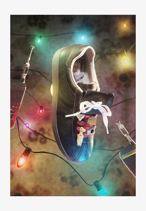 Fekete sneaker fehér fűzőkkel, kitűzőkkel feldíszítve, színes karácsonyi fények és két walkie-talkie veszik körül.