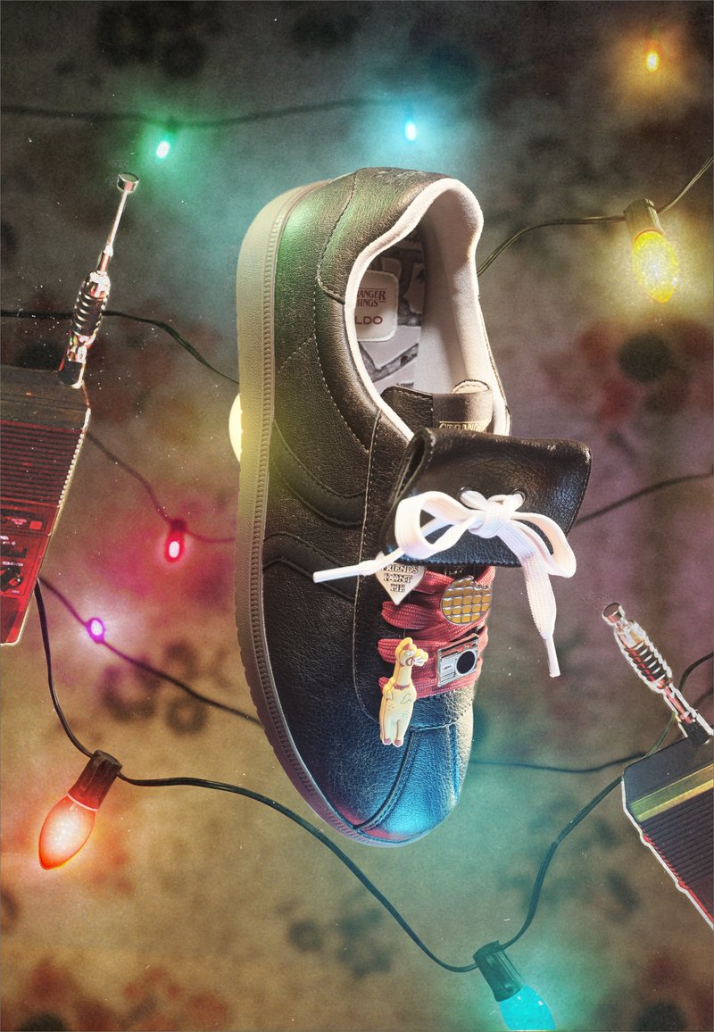 Fekete sneaker fehér fűzőkkel, kitűzőkkel feldíszítve, színes karácsonyi fények és két walkie-talkie veszik körül.