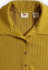 Gulrandig kortärmad skjorta med bred krage och fem bruna knappar, med texturerad tyg och Levi's etikett i halsringningen.