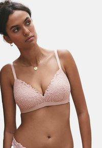 Lyserød blonde bralette med trekantet form, bølgede kanter og justerbare stropper. Har blomsterprint og en blød stofstruktur.