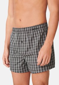 Boxers noirs et gris à carreaux en tissu léger, dotés d'une taille élastique et d'une fermeture à un bouton à l'avant.