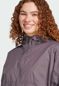 Lättviktsjacka med huva i mauve tyg med en slät yta, utrustad med dragkedja fram och dragsko vid kragen för justering.