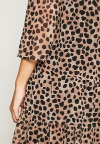 Robe à manches courtes à imprimé animal beige et noir vue de dos, avec une jupe à volants superposés et un bras partiellement visible.