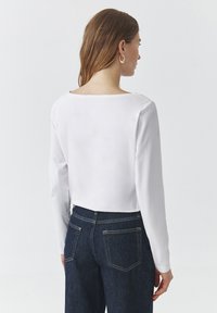 Cămașă albă cu mâneci lungi și decolteu larg, asociată cu blugi din denim de un albastru închis, cu un croi clasic și buzunare la spate.