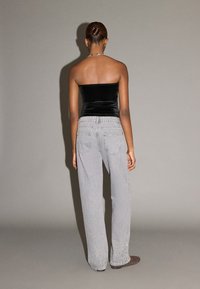 Top negru din catifea, fără bretele, asortat cu blugi largi de culoare gri deschis, cu spălare estompată și buzunare în spate. Textură netedă și croială lejeră.