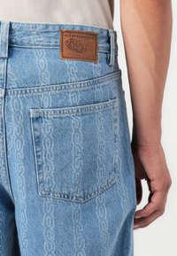 Lichtblauwe denim jeans met een subtiel kettingpatroon, een bruine leren label met "element" op de tailleband en een klassieke vijf-zakken ontwerp.