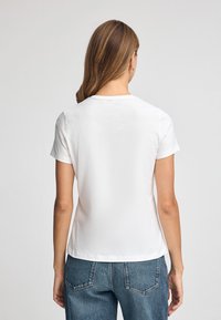 Vit kortärmad T-shirt med rundad halsringning, slät textur och rak passform. Kombinerad med höga jeans.